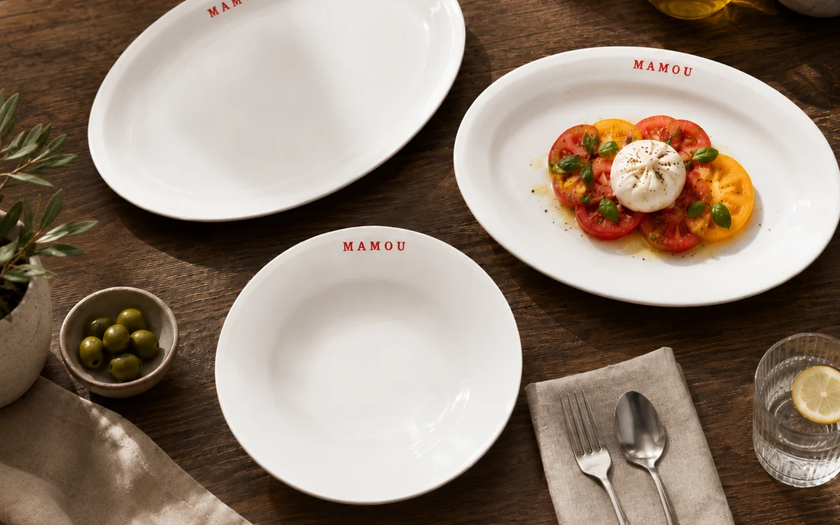 A Mamou-branded platter, plate and bowl laid on a table with a tomato and burrata salad